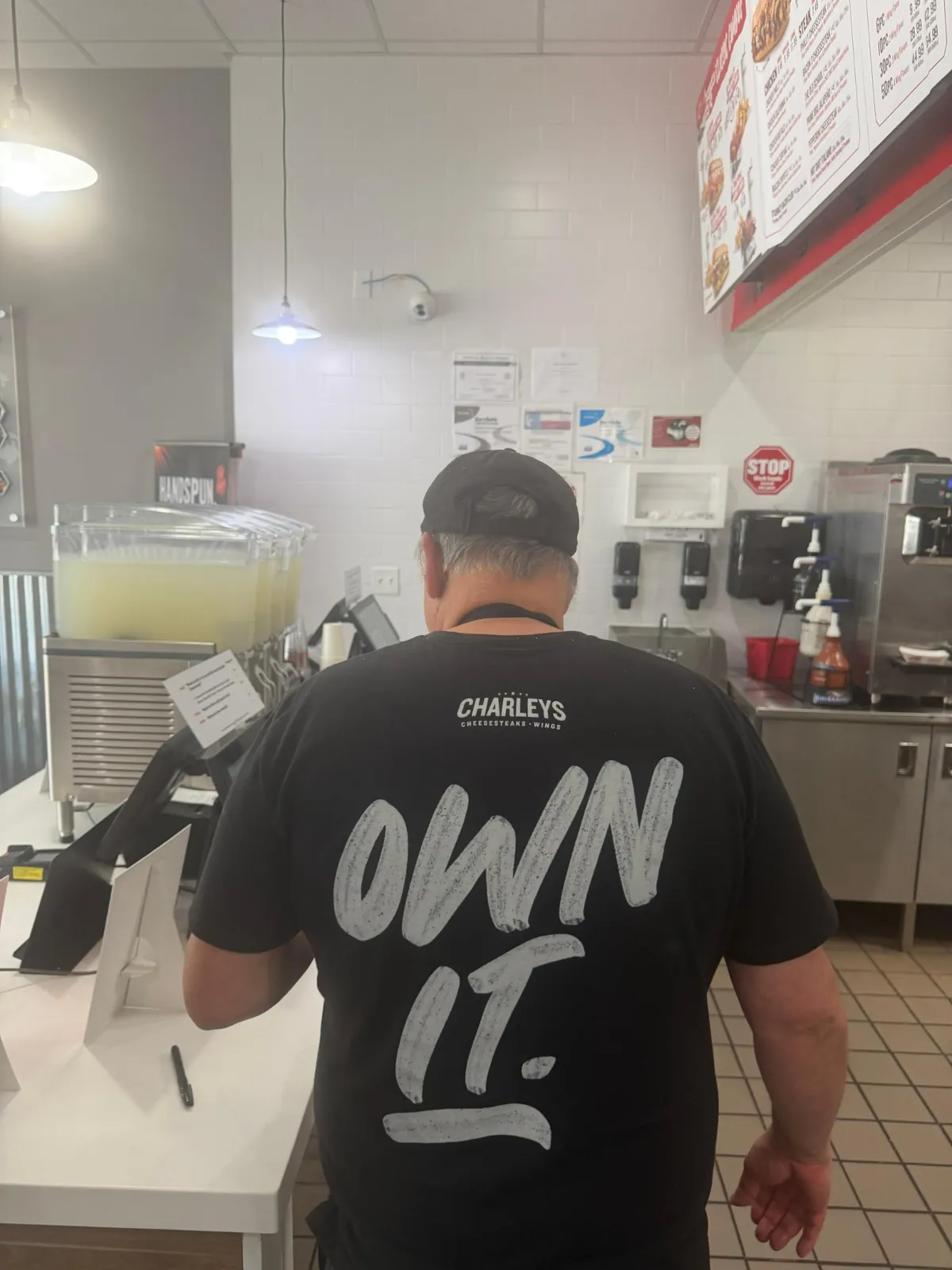 Real-world Charleys restaurant observation showing the words Own It on a shirt